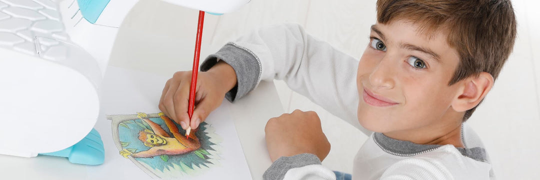 A smiling kid is looking towards you while drawing a monkey hanging from a tree using the smART sketcher® Projector 2.0